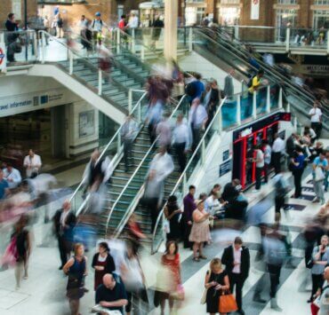 We see a flurry of shoppers walking in and out of retail outlets in a mall.